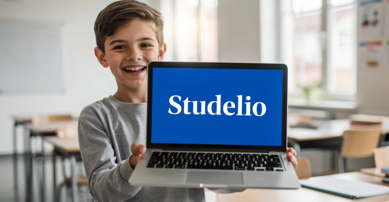 Un collégien souriant tient son ordinateur portable, sur lequel est inscrit "Studelio" en blanc sur un fond bleu vif. Le jeune élève exprime sa joie et son enthousiasme pour ses cours et ses exercices de français.