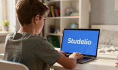 Un collégien de 12 ans est assis devant son ordinateur, concentré sur son travail. L'écran affiche le mot "Studelio" en blanc sur un fond bleu vif, illustrant une activité d'apprentissage qui pourrait aider les enfants à développer leurs compétences pendant les vacances.