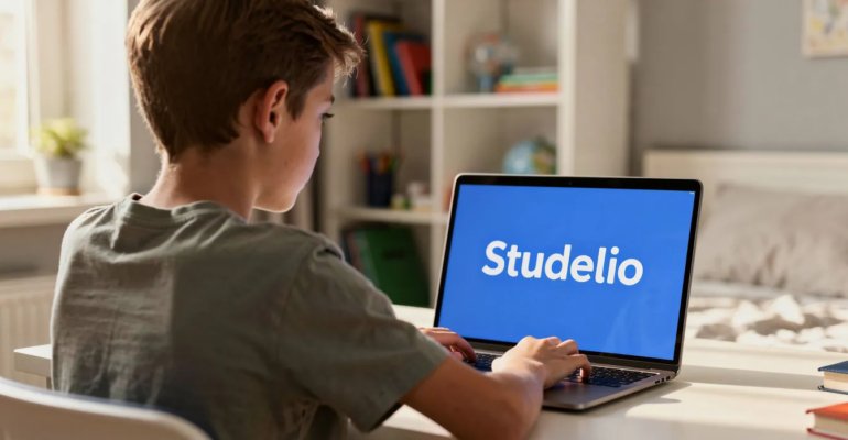 Un collégien de 12 ans est assis devant son ordinateur, concentré sur son travail. L'écran affiche le mot "Studelio" en blanc sur un fond bleu vif, illustrant une activité d'apprentissage qui pourrait aider les enfants à développer leurs compétences pendant les vacances.